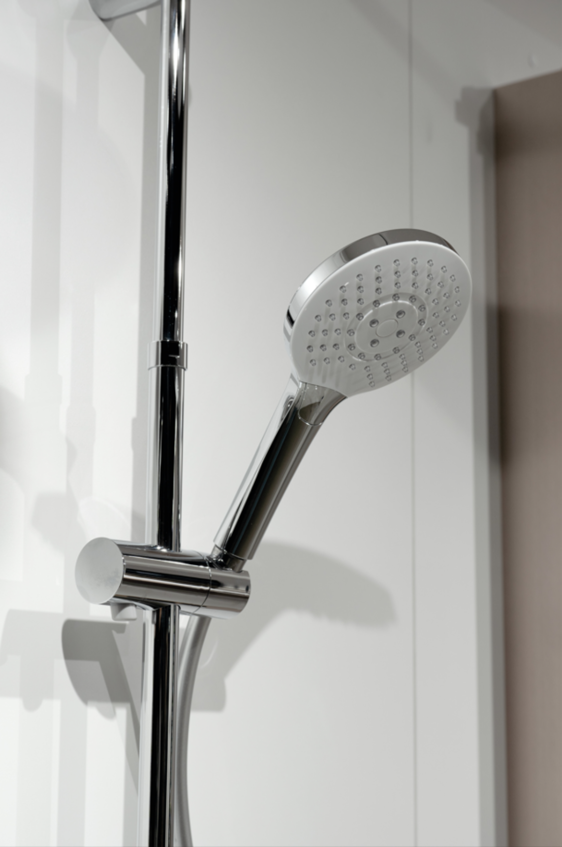 Gros plan sur une douchette à main ronde chromée avec plusieurs buses de jet, installée sur une barre de douche réglable en hauteur.