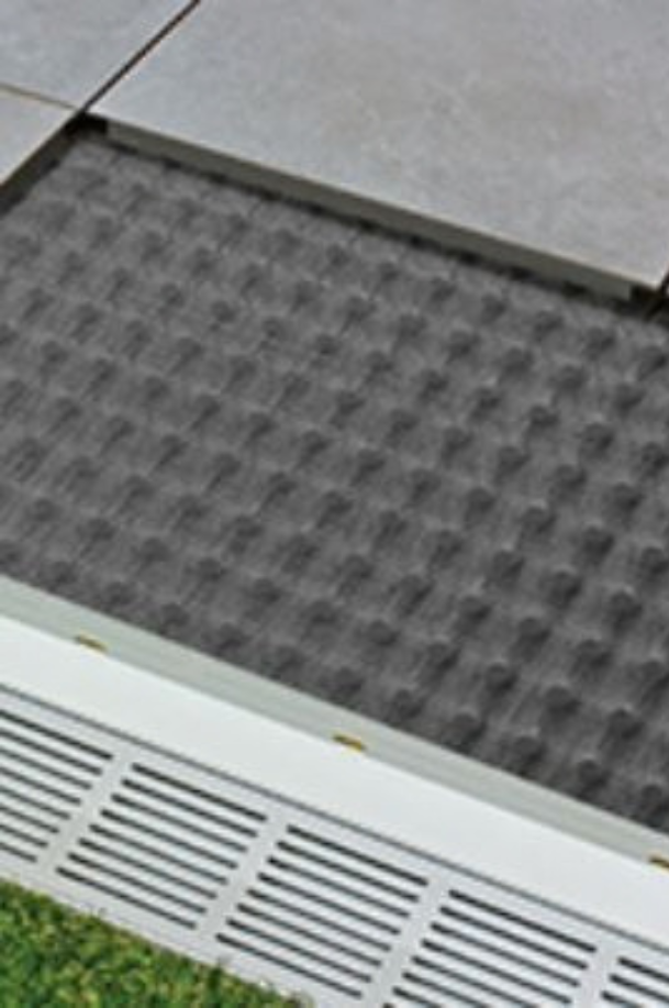 Illustration technique d'une natte de désolidarisation grise sous un carrelage de sol, à proximité d'un caniveau de drainage.