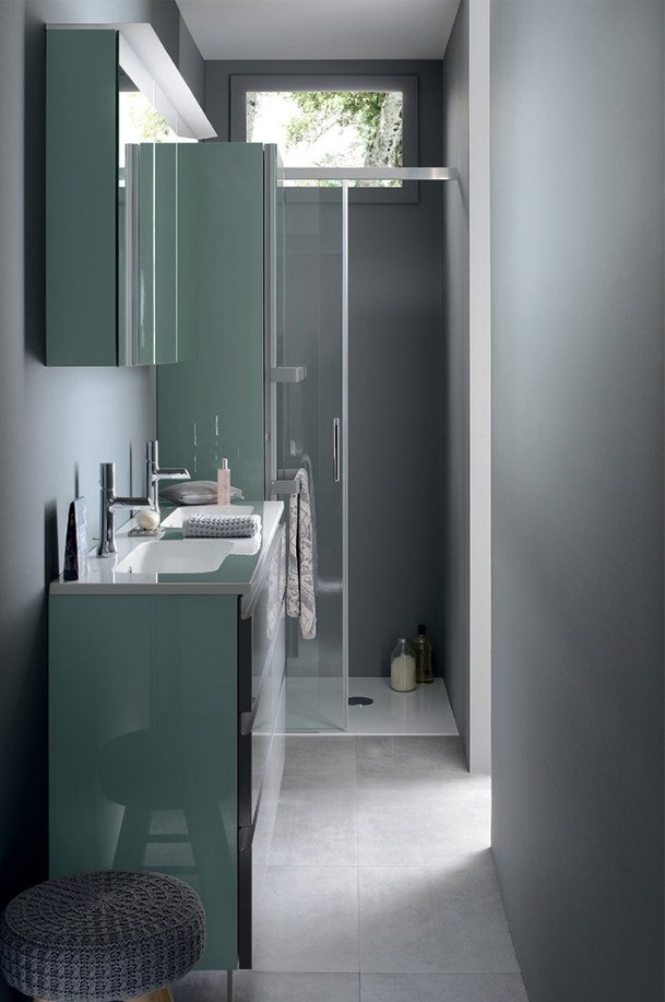 Aménagement d’une petite salle de bains étroite avec meuble vasque vert, armoire miroir et douche vitrée au fond de la pièce.